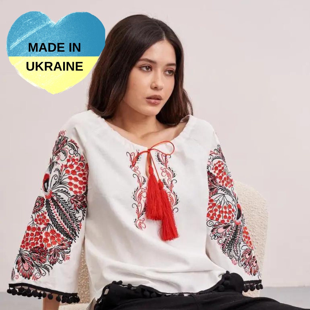 a woman sitting on a chair wearing a white top with a red tassel