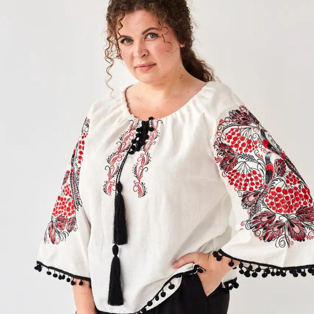 a woman wearing a white blouse with red and black designs