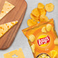 a bag of lays chips next to a wooden cutting board