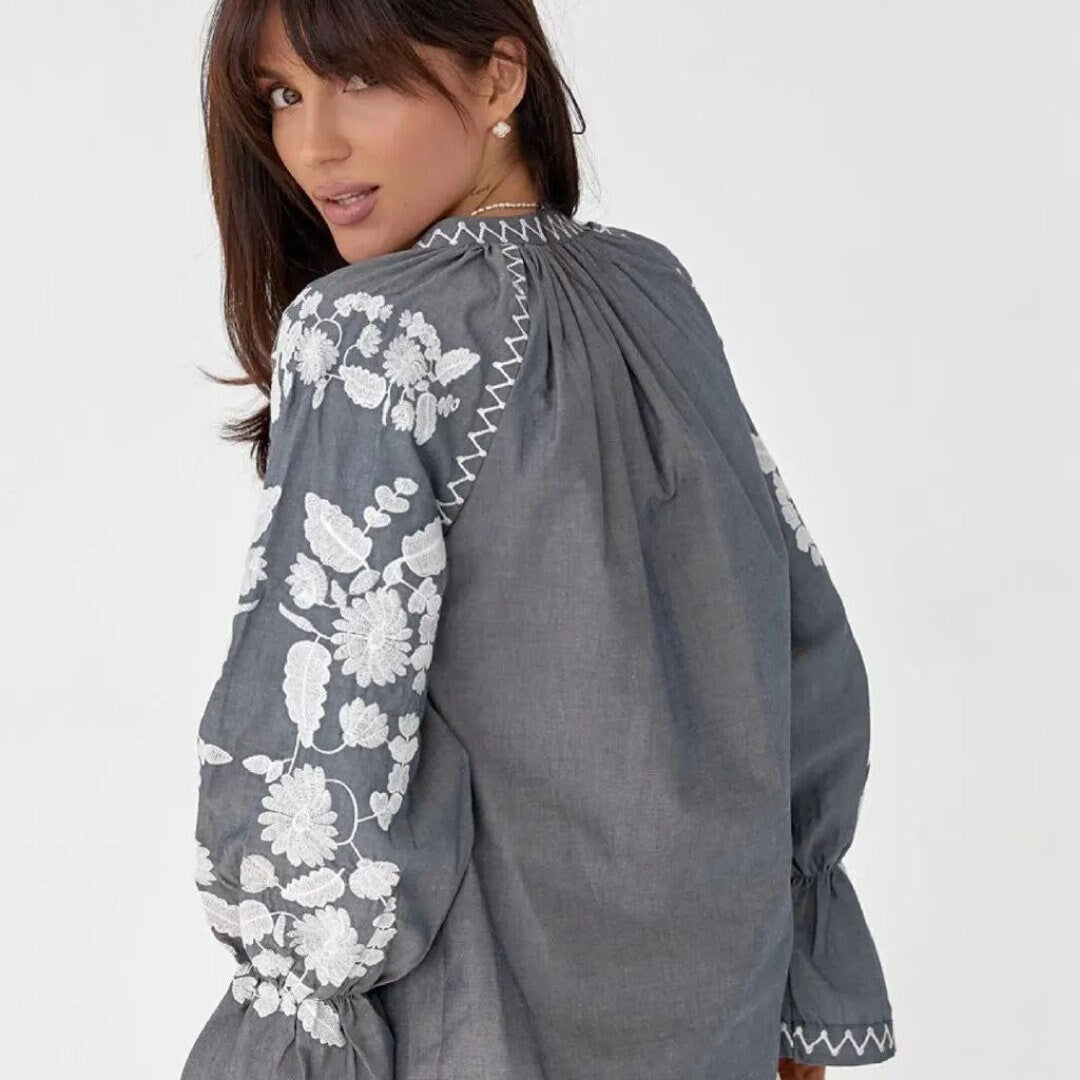 a woman wearing a grey blouse with white flowers on it