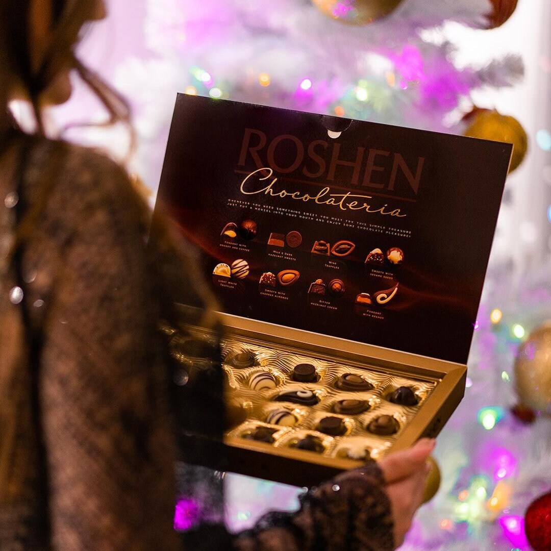 a woman holding a box of chocolates in front of a christmas tree