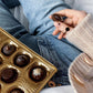 a person sitting on a bed with a tray of chocolates