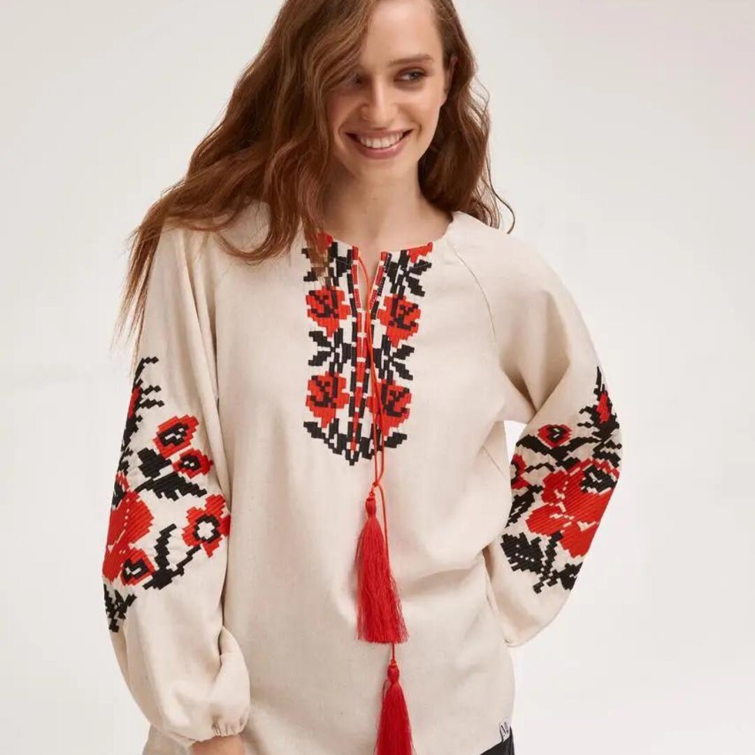 a woman wearing a white top with red flowers and tassels