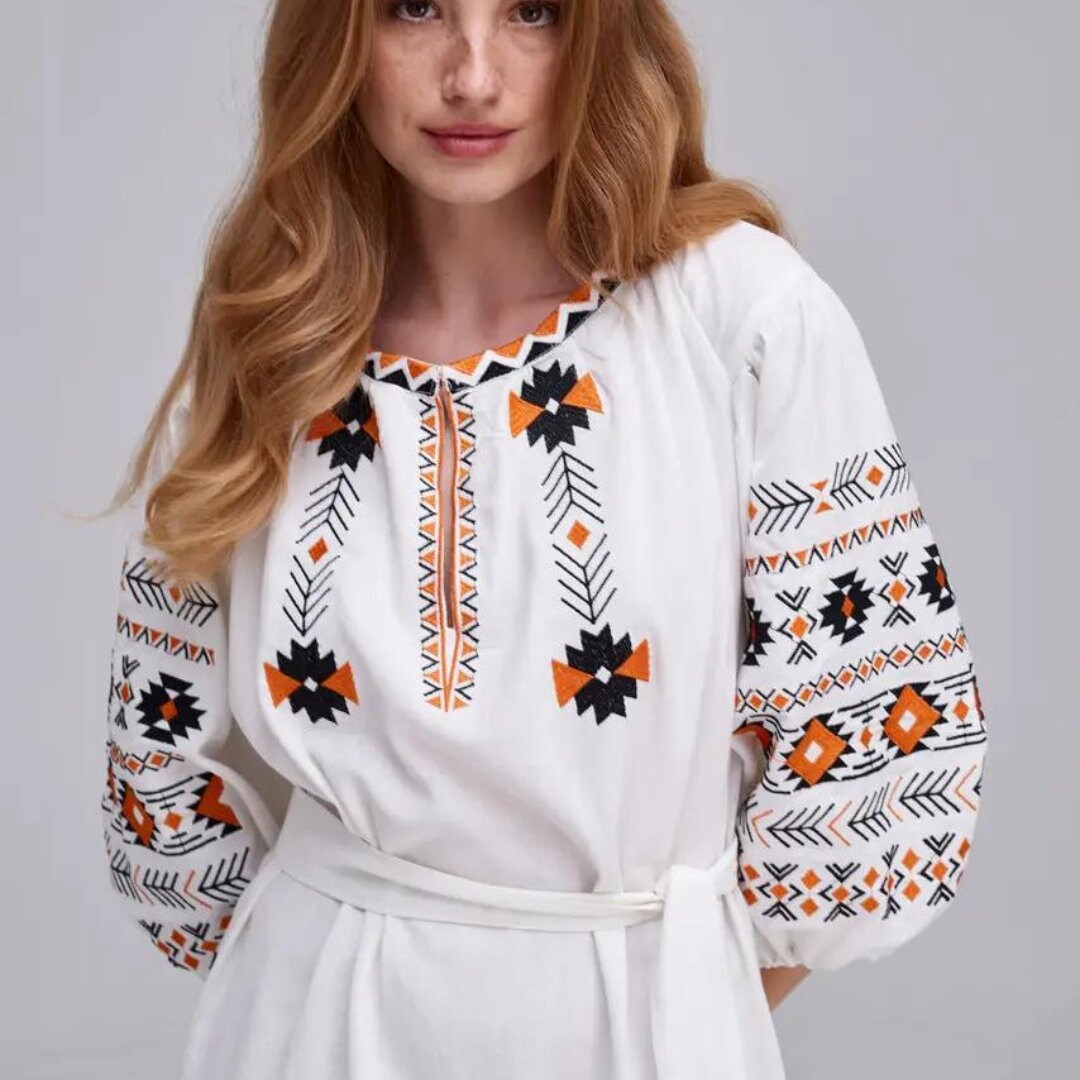 a woman wearing a white dress with an orange and black design