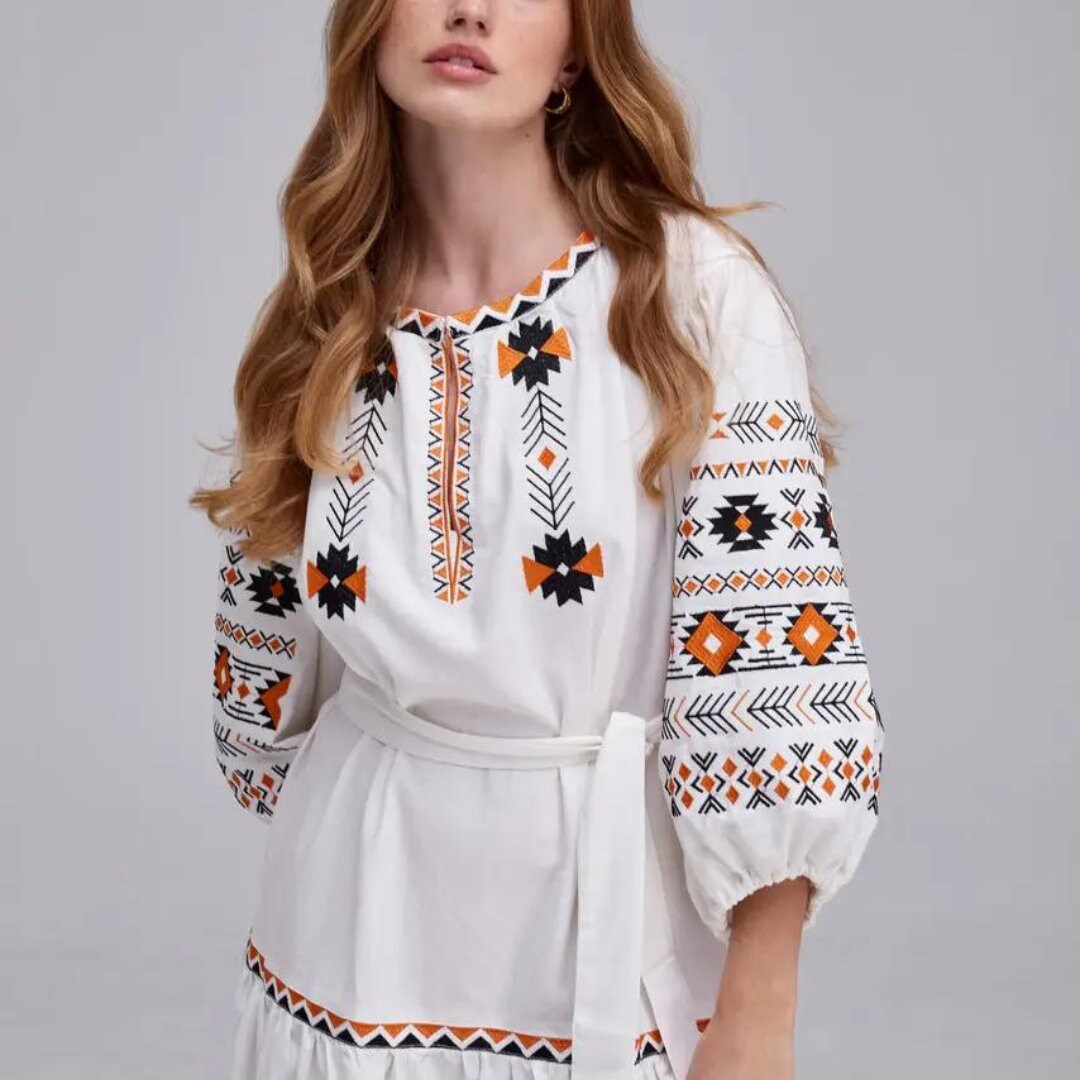 a woman wearing a white dress with an orange and black design