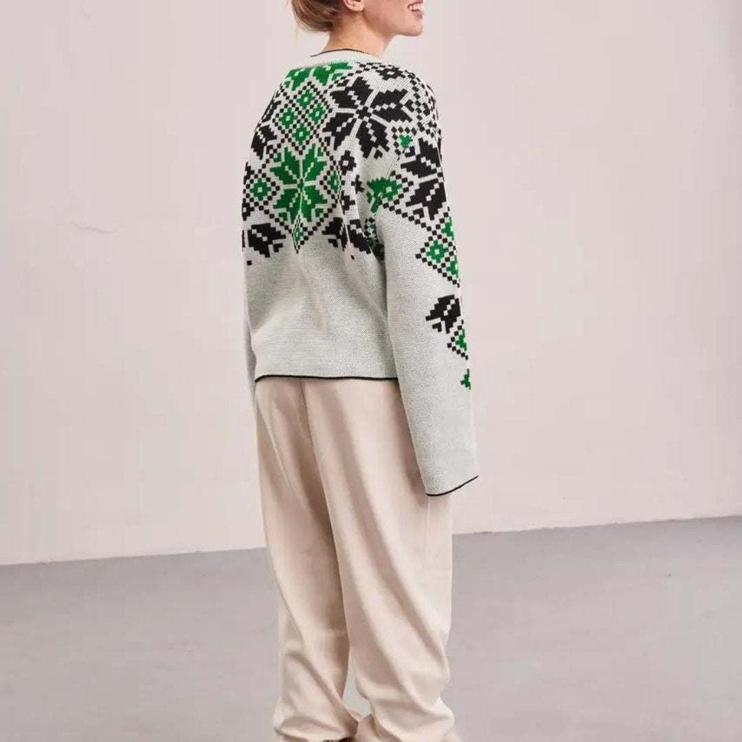 a woman in a sweater and pants standing in front of a white wall