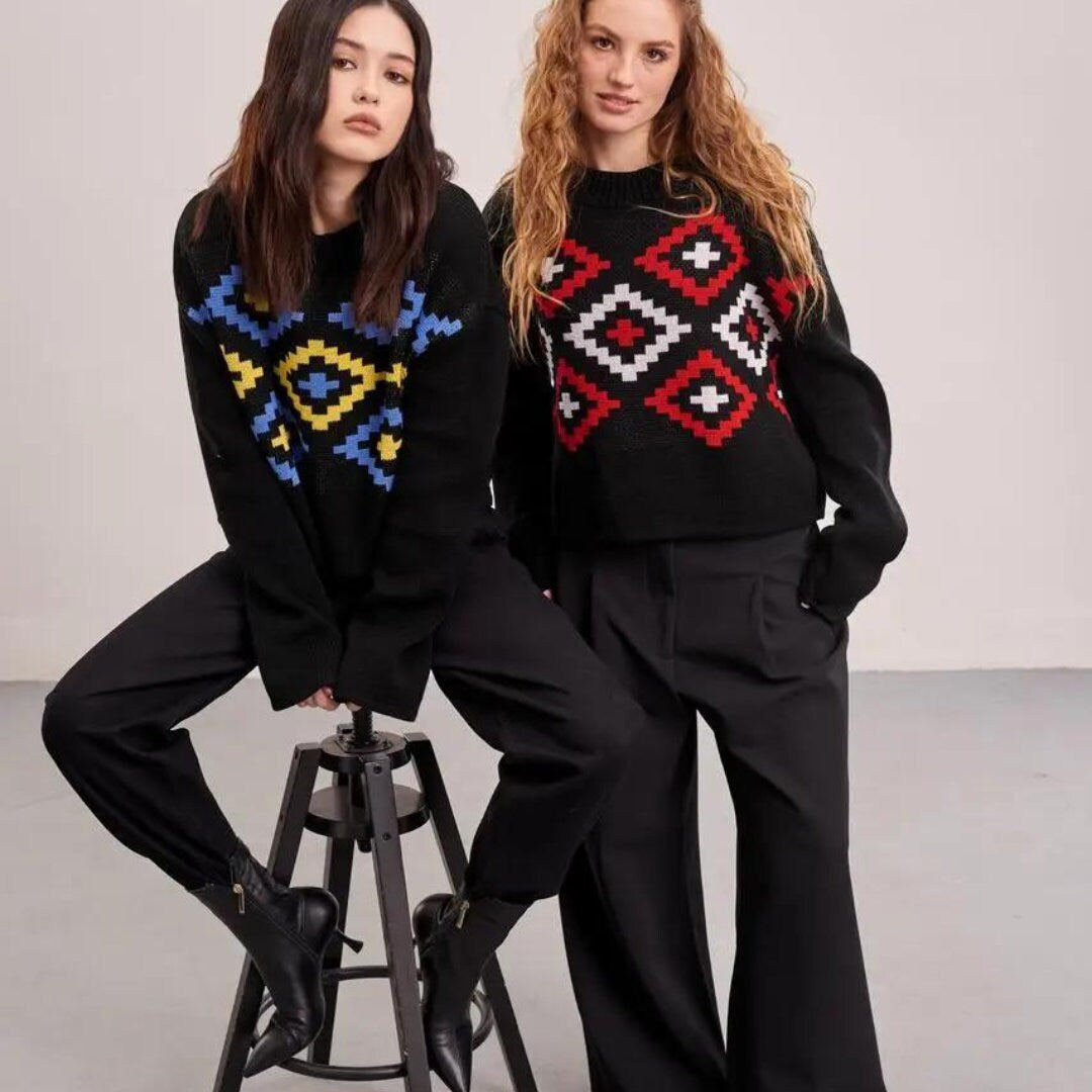 two women in sweaters sitting on a stool