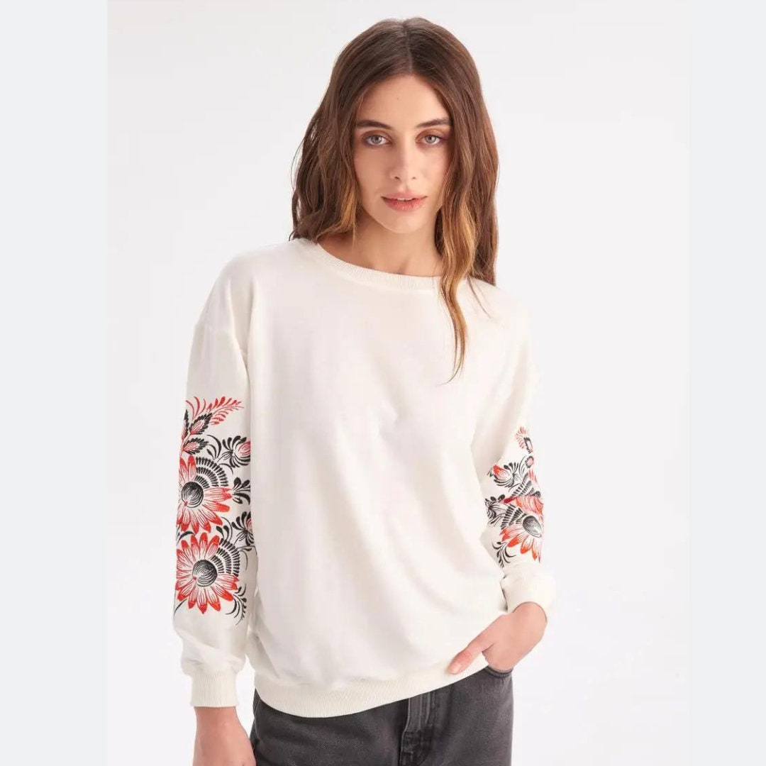 a woman wearing a white sweater with red flowers on it