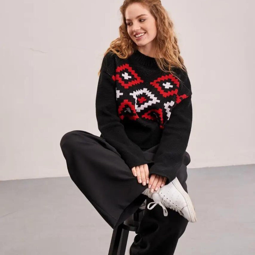 a woman sitting on a stool wearing a black sweater and black pants