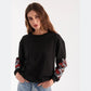 a woman wearing a black sweatshirt with red flowers on the sleeves